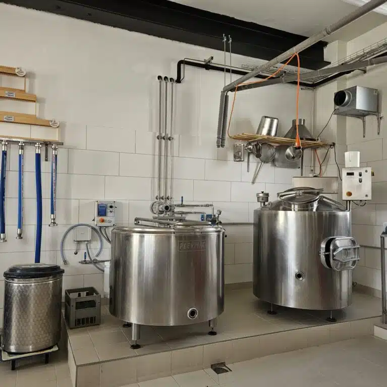 Intérieur d'un laboratoire de production avec des cuves en acier inoxydable, des tuyaux bleus, un système de filtration et divers équipements de brassage.