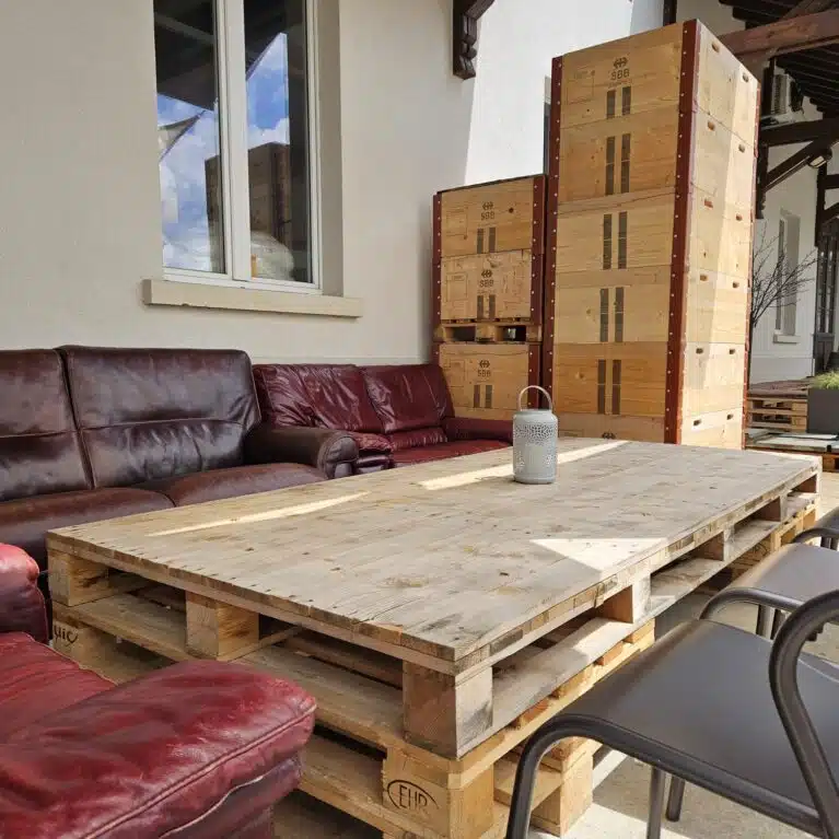 Espace extérieur accueillant avec des canapés en cuir rouge, une table en palettes en bois et des chaises noires. L'ambiance est moderne et conviviale, idéale pour se détendre.
