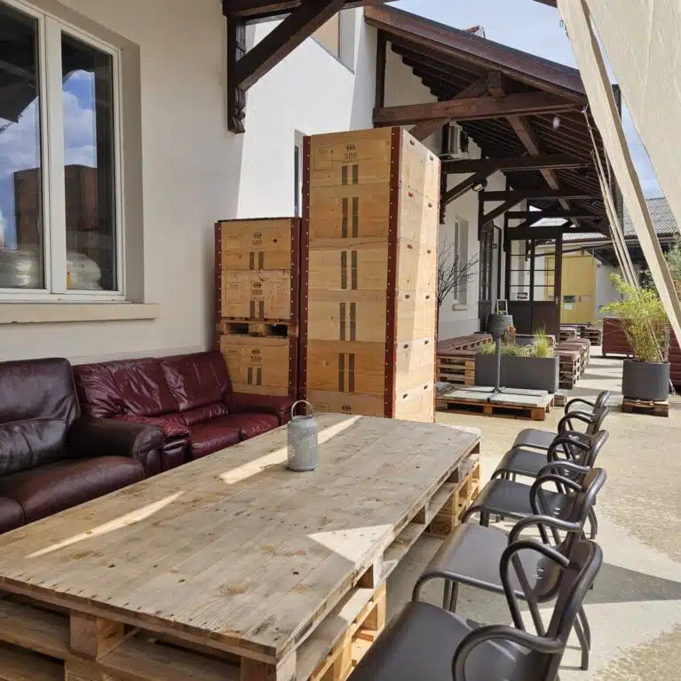 Espace extérieur confortable avec un salon en cuir, une grande table en bois, et des chaises noires, idéal pour se détendre ou recevoir des invités.